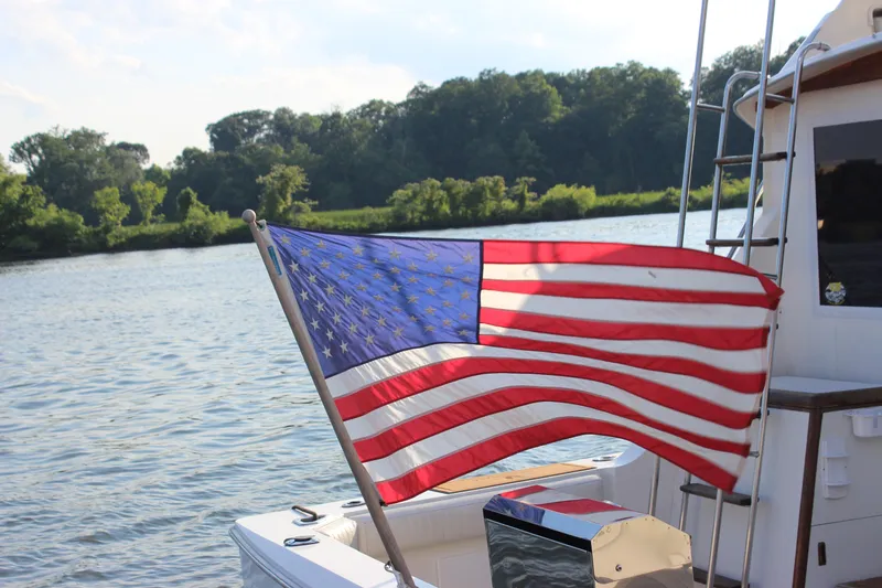 Slide: The Image of American flag on 1988 Bertram 33II Flybridge Cruiser, river backdrop. - 11