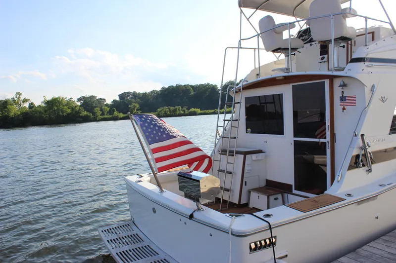 Slide: The Image of 1988 Bertram 33II Flybridge Cruiser docked by a serene river with an American flag. - 12