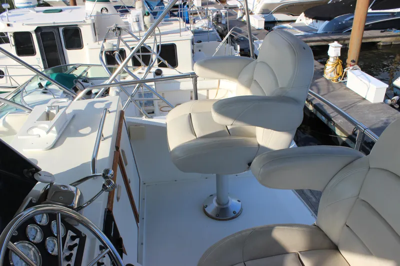 Slide: The Image of 1988 Bertram 33II Flybridge Cruiser helm with white captain chairs at marina. - 38