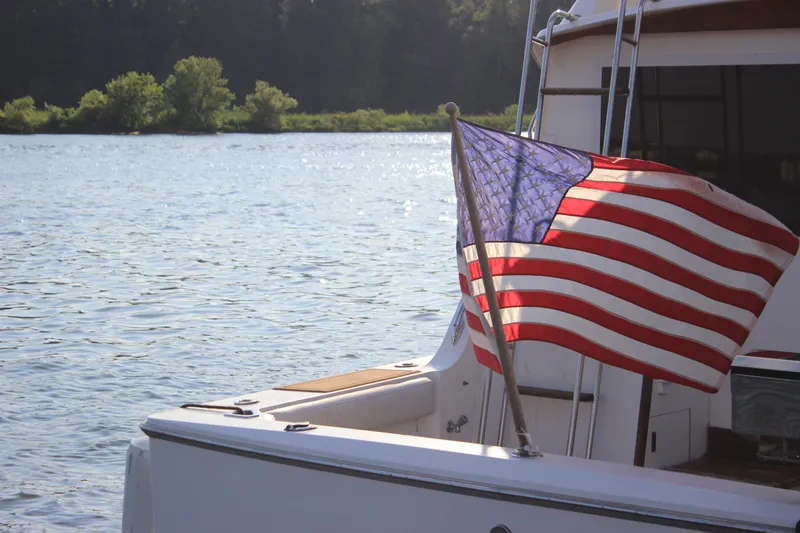 Slide: The Image of 1988 Bertram 33II Flybridge Cruiser with American flag on a serene lake. - 9