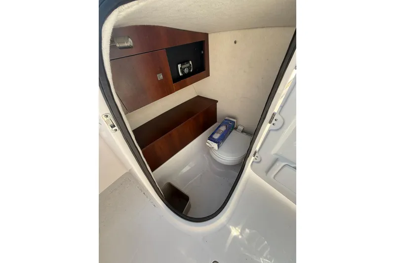Slide: The Image of 2019 Robalo R227 Dual Console boat interior with compact toilet and wooden cabinetry. - 8