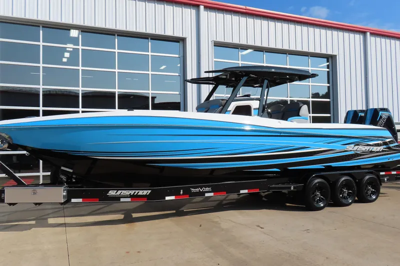 Slide: The Image of 2024 Sunsation 32CCX boat in blue, parked on a trailer outside a garage. - 2