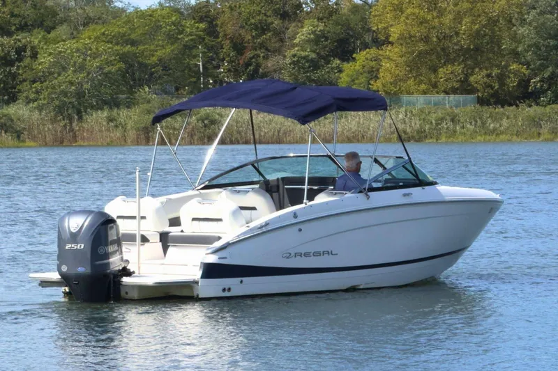 The Image of 2023 Regal LX4 boat with blue canopy cruising on a serene lake. - 0