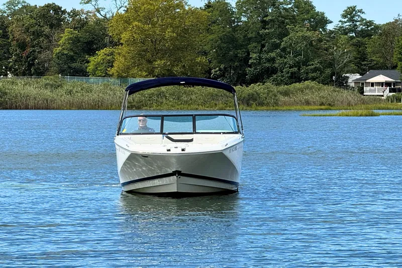 Slide: The Image of 2022 Regal 23 OBX boat cruising on a serene lake with lush greenery. - 6