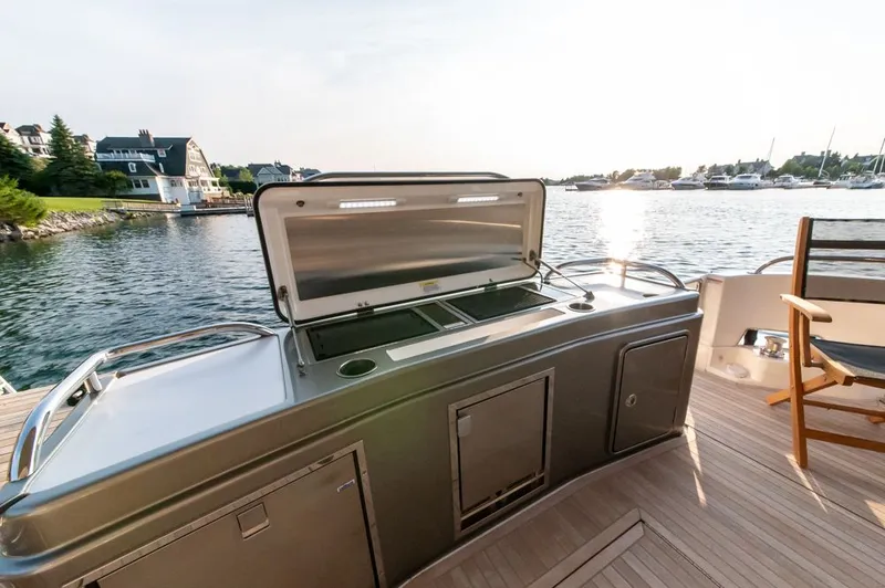 Slide: The Image of 2022 Riviera 6000 Sport Yacht Platinum with outdoor kitchen, docked by waterfront homes. - 18
