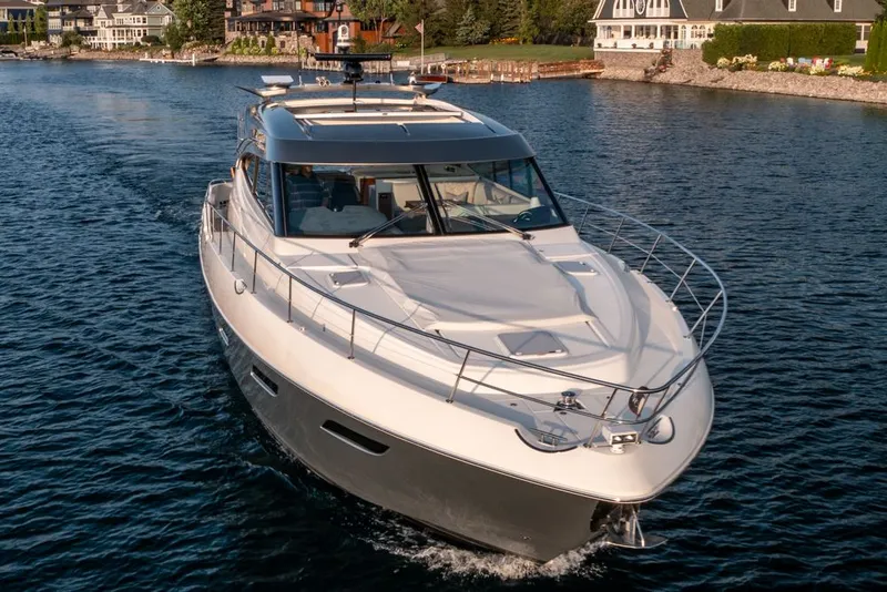 Slide: The Image of 2022 Riviera 6000 Sport Yacht Platinum cruising on a serene lake near luxury homes. - 2