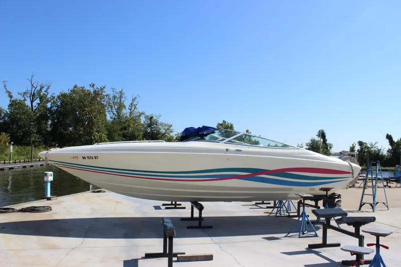 The Image of 1995 Baja 272 speedboat on stands, vibrant stripes, clear sky background. - 0