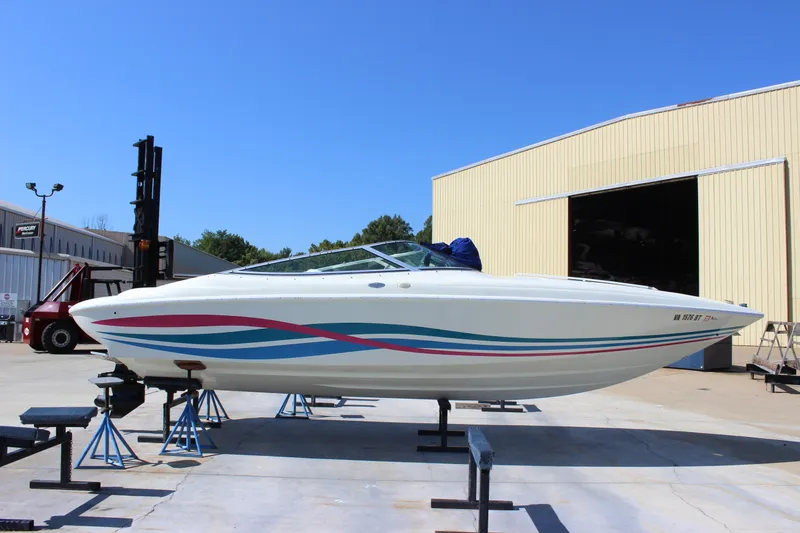 Slide: The Image of 1995 Baja 272 boat on stands, vibrant stripes, parked outside a large warehouse. - 7