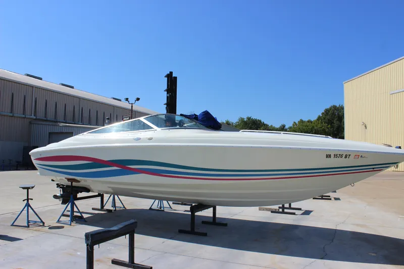 Slide: The Image of 1995 Baja 272 speedboat on stands, featuring colorful stripes, parked outdoors. - 8