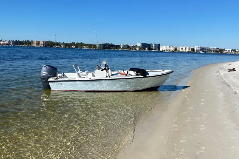 The Image of 1989 Mako 171 Center Console boat on sandy beach with clear water and cityscape background. - 0