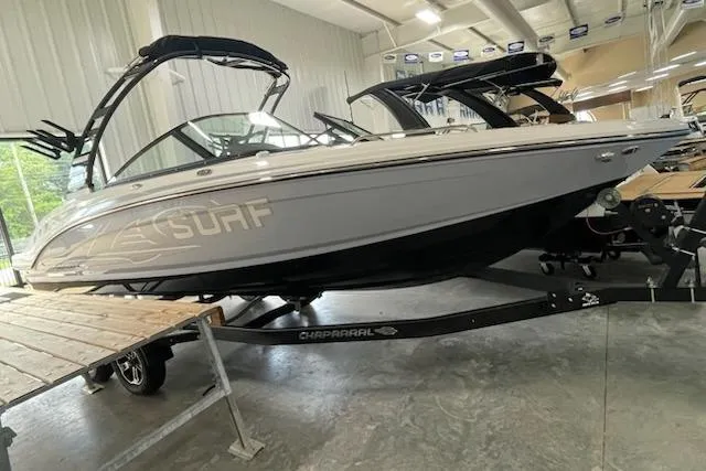 The Image of 2025 Chaparral 23 Surf boat displayed indoors on a trailer. - 0