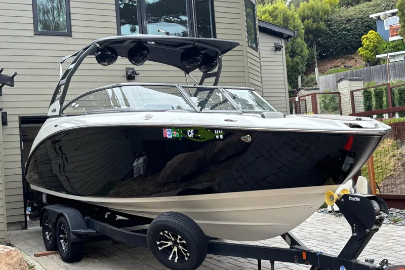 Slide: The Image of 2022 Yamaha Boats 252S on trailer, parked near modern house, surrounded by greenery. - 2