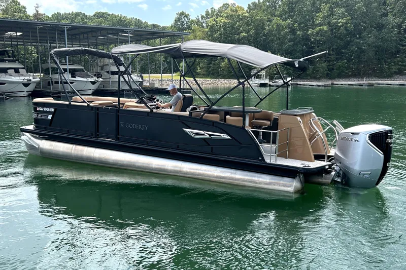 Slide: The Image of 2025 Godfrey AquaPatio Entertainment 255 CBE pontoon boat on a serene lake. - 2