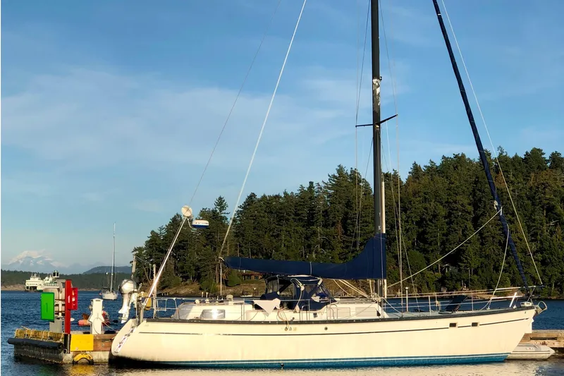 The Image of 1987 Cascade Center Cockpit sailboat docked by forested shoreline. - 0