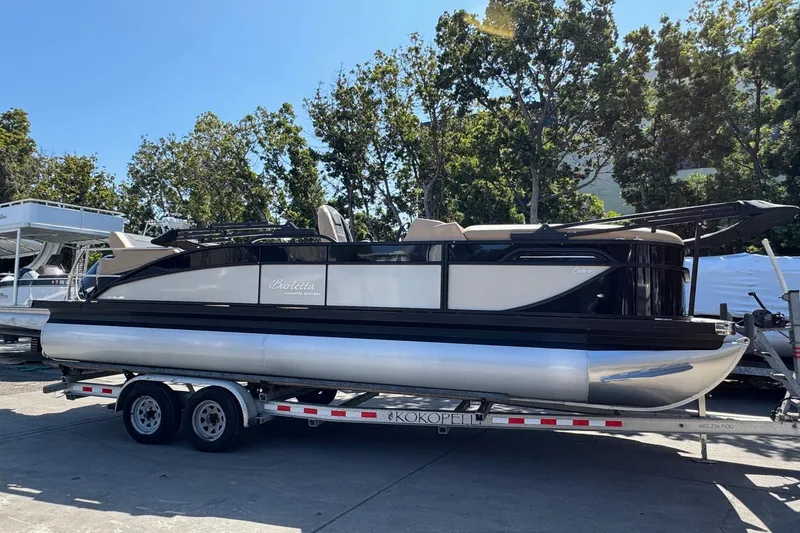 Slide: The Image of 2026 Barletta Cabrio 24UE pontoon boat with canopy on trailer, surrounded by trees. - 2