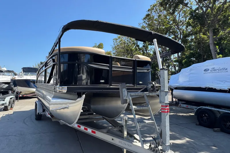 Slide: The Image of 2026 Barletta Cabrio 24UE pontoon boat on trailer, parked outdoors under clear blue sky. - 7