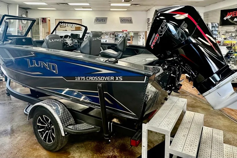 Slide: The Image of 2026 Lund 1875 Crossover XS boat in showroom, featuring sleek design and powerful engine. - 3