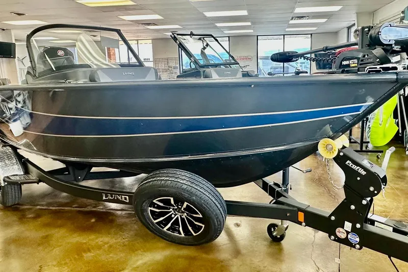 Slide: The Image of 2026 Lund 1875 Crossover XS boat on trailer in showroom, featuring sleek black design. - 6