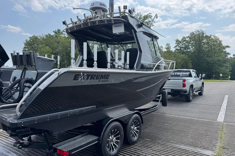 Slide: The Image of 2023 Extreme Boats 795 Game King on trailer, parked near a truck in a scenic area. - 27