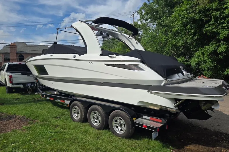 Slide: The Image of 2023 Four Winns H290 boat on trailer, parked outdoors with lush greenery. - 2