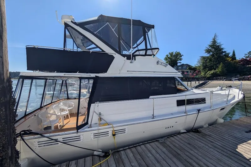 The Image of 1989 Bayliner 3888 Motoryacht docked, featuring spacious deck and upper helm, under clear blue sky. - 0