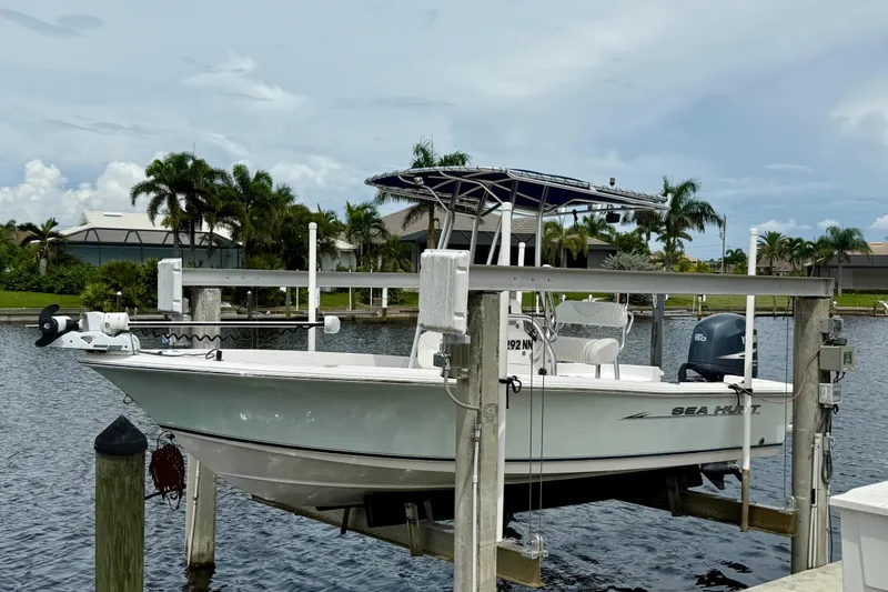 The Image of 2007 Sea Hunt BX 21 T boat on lift by waterfront, surrounded by palm trees. - 0