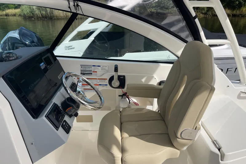 Slide: The Image of 2020 Pursuit DC 235 Dual Console boat interior with steering wheel and beige captain's chair. - 15