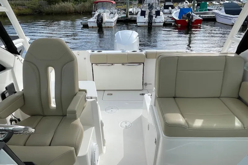 Slide: The Image of 2020 Pursuit DC 235 Dual Console boat interior with beige seating at a marina. - 32