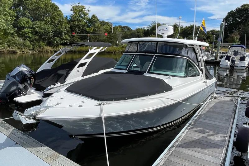 Slide: The Image of 2020 Pursuit DC 235 Dual Console boat docked at marina, surrounded by trees and other boats. - 60