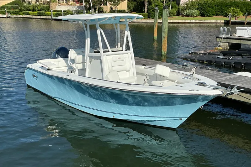 Slide: The Image of 2019 Sea Hunt Ultra 225 boat docked in calm waters, featuring a sleek blue hull. - 7