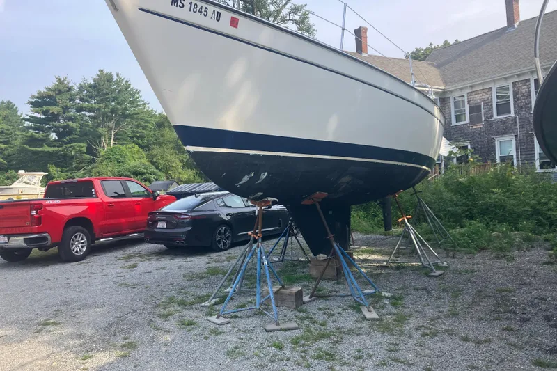 The Image of 1983 Pearson 303 Sloop sailboat on stands, parked near red and black vehicles. - 0