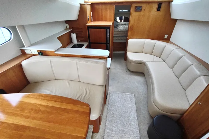 Slide: The Image of 2003 Silverton 330 Sport Bridge interior with beige seating, wooden accents, and compact kitchen area. - 12