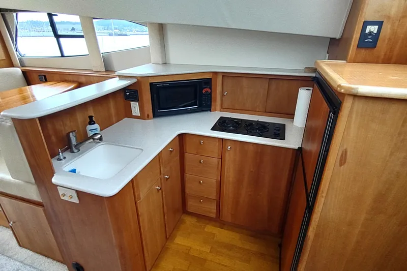 Slide: The Image of 2003 Silverton 330 Sport Bridge yacht kitchen with sink, stove, microwave, and wooden cabinetry. - 16