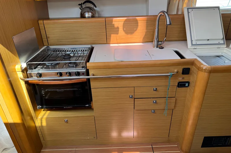 Slide: The Image of 2009 Jeanneau Sun Odyssey 44i yacht kitchen with stove, sink, and wooden cabinetry. - 17