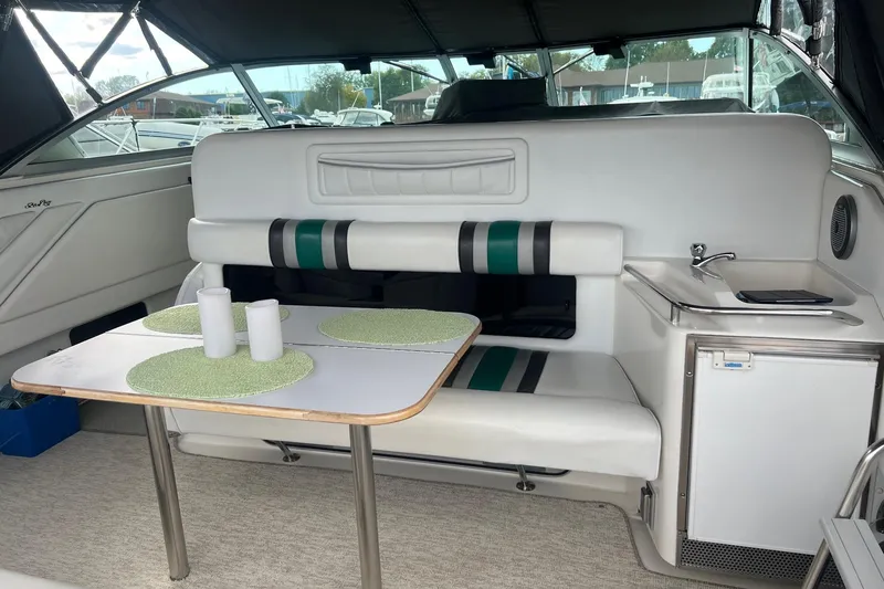 Slide: The Image of 1990 Sea Ray 350 Sundancer interior with dining area, table, and compact kitchenette. - 4