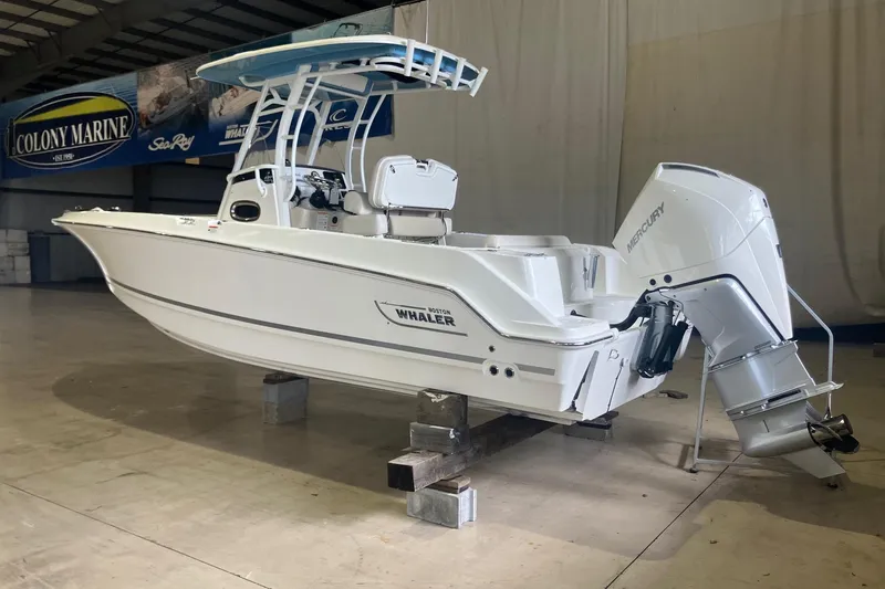 Slide: The Image of 2026 Boston Whaler 230 Outrage boat in showroom, featuring Mercury outboard engine. - 2