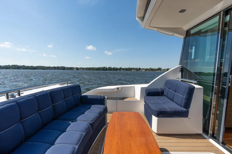 Slide: The Image of 2015 Tiara Yachts C44 Coupe deck with blue seating and wooden table, overlooking water. - 39