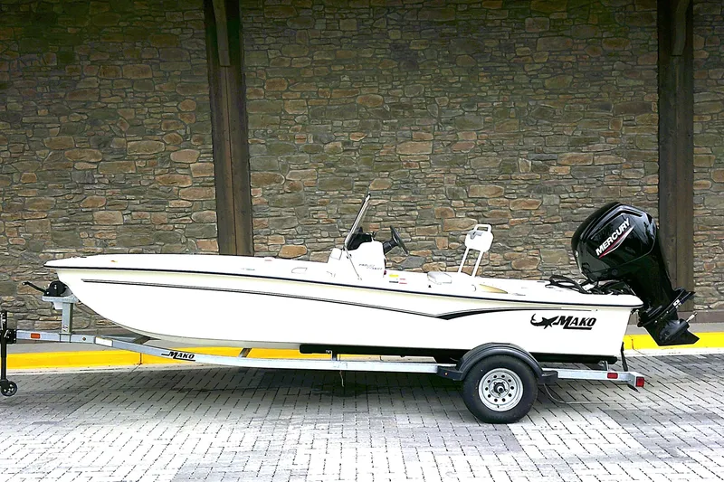Slide: The Image of 2026 Mako Pro Skiff 17 CC boat on trailer, parked by stone wall. - 1