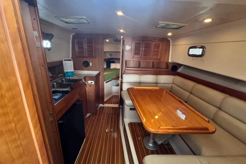 Slide: The Image of 2003 Mainship Pilot 34 interior with wooden table, beige seating, and compact kitchen area. - 19
