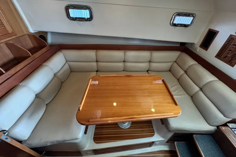 Slide: The Image of 2003 Mainship Pilot 34 interior with beige cushioned seating and wooden table. - 20