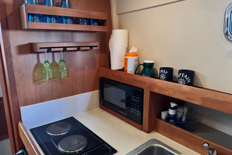 Slide: The Image of 2003 Mainship Pilot 34 galley with stove, microwave, and glassware storage. - 24