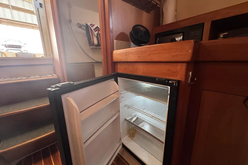 Slide: The Image of 2003 Mainship Pilot 34 interior with open mini fridge and wooden cabinetry. - 26