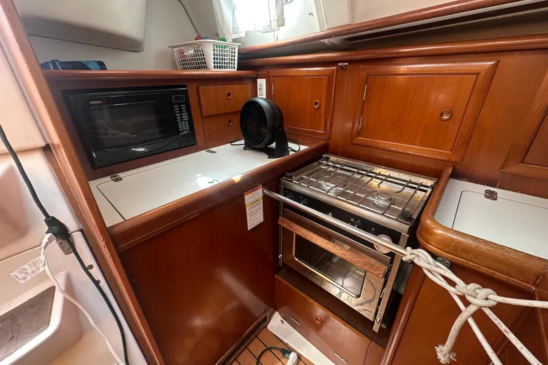 Slide: The Image of 2003 Beneteau Oceanis Clipper 331 yacht kitchen with microwave, stove, and wooden cabinetry. - 37