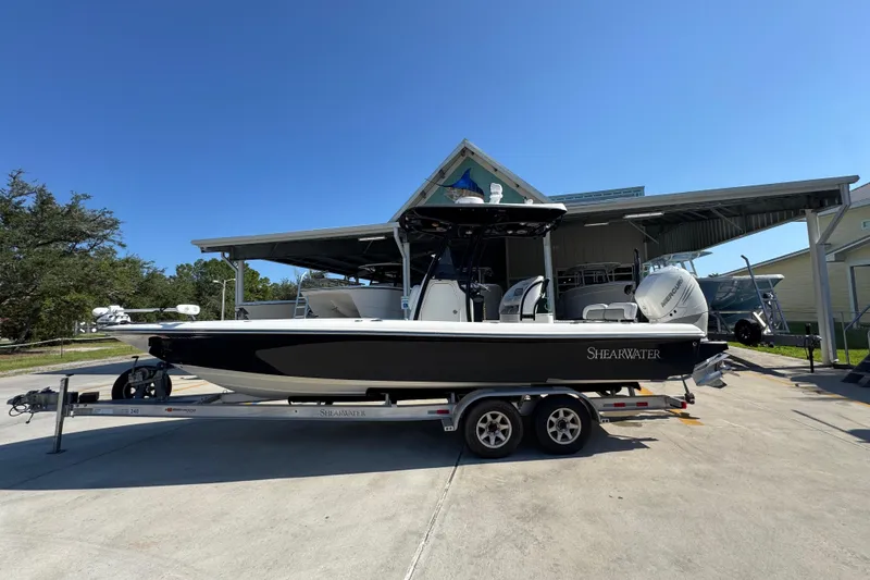 The Image of 2013 ShearWater 27 LTZ boat on trailer, parked outdoors under clear blue sky. - 1