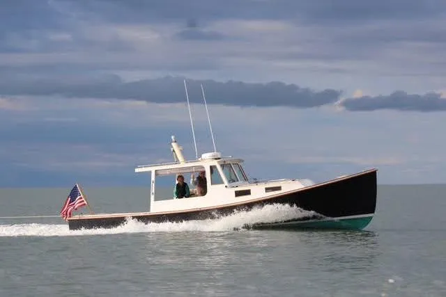 The Image of 1995 Holland Pettegrow Cruiser on calm sea with American flag, under cloudy sky. - 0