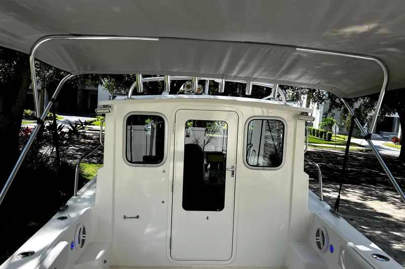 Slide: The Image of 2023 Parker 2120 Sport Cabin boat with canopy, rear view in a shaded outdoor setting. - 22