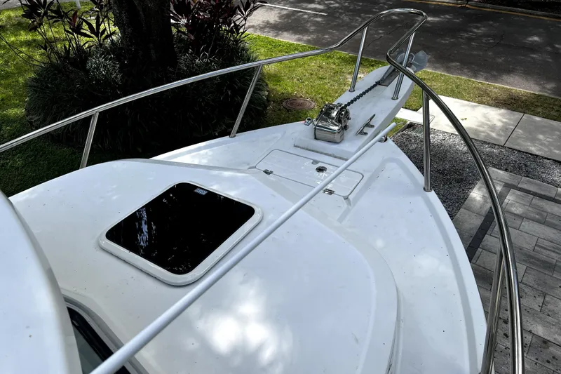 Slide: The Image of 2023 Parker 2120 Sport Cabin boat deck with railing and hatch, parked near greenery. - 58