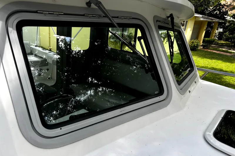 Slide: The Image of 2023 Parker 2120 Sport Cabin boat with reflective windows and lush surroundings. - 64
