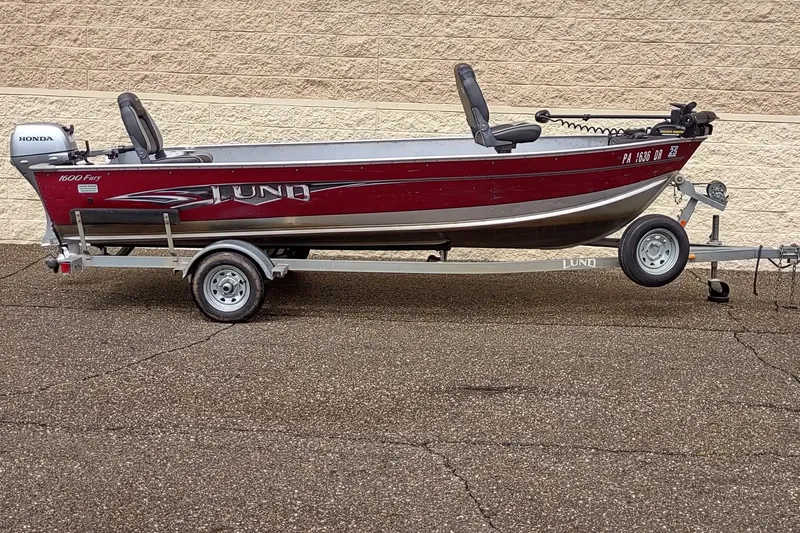 Slide: The Image of 2015 Lund 1600 Fury Tiller boat on trailer, red and silver design, parked outdoors. - 0