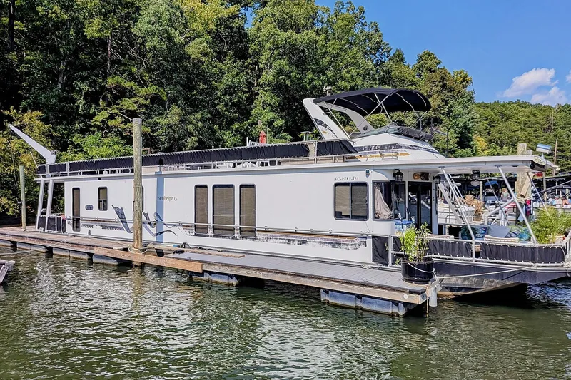 The Image of 1996 Stardust Cruisers houseboat docked on a serene lake with lush greenery. - 0